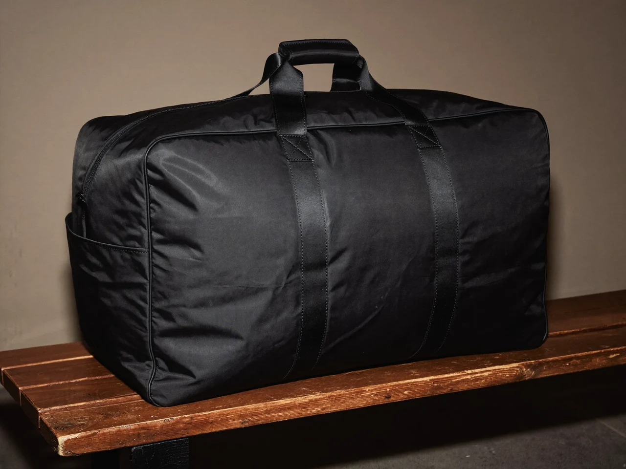 Grand duffel noir avec poche latérale pour chaussures, posé sur un banc de vestiaire